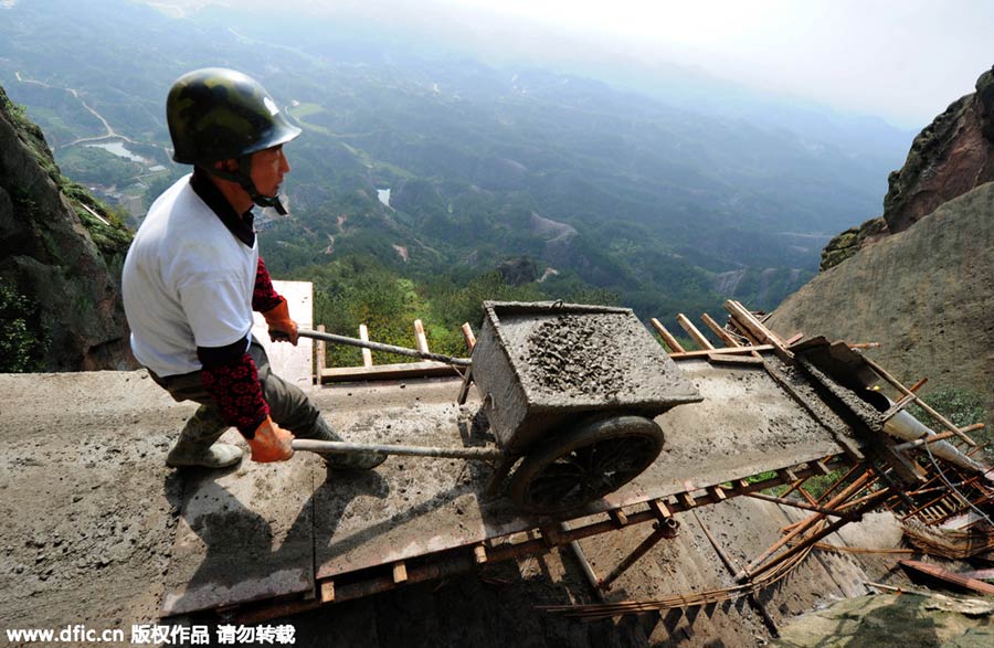 Workers balance on planks to build mountain road