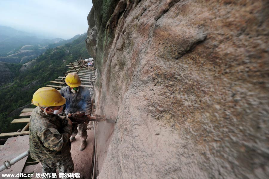 Workers balance on planks to build mountain road
