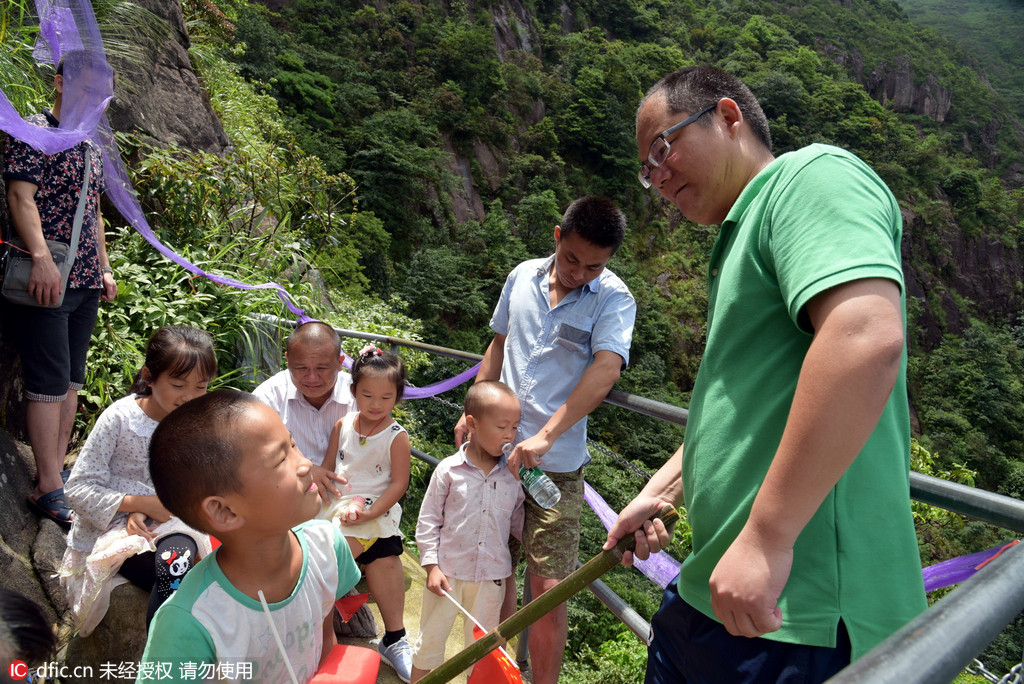 Fathers use bamboo strips to steer children on cliff walkway